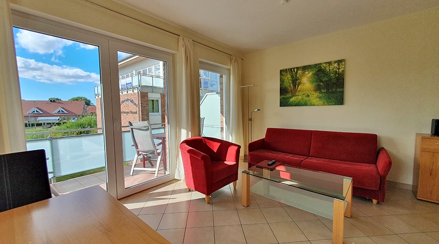 Wohnzimmer mit rotem Sofa, Sessel und offener Küche mit Esstisch